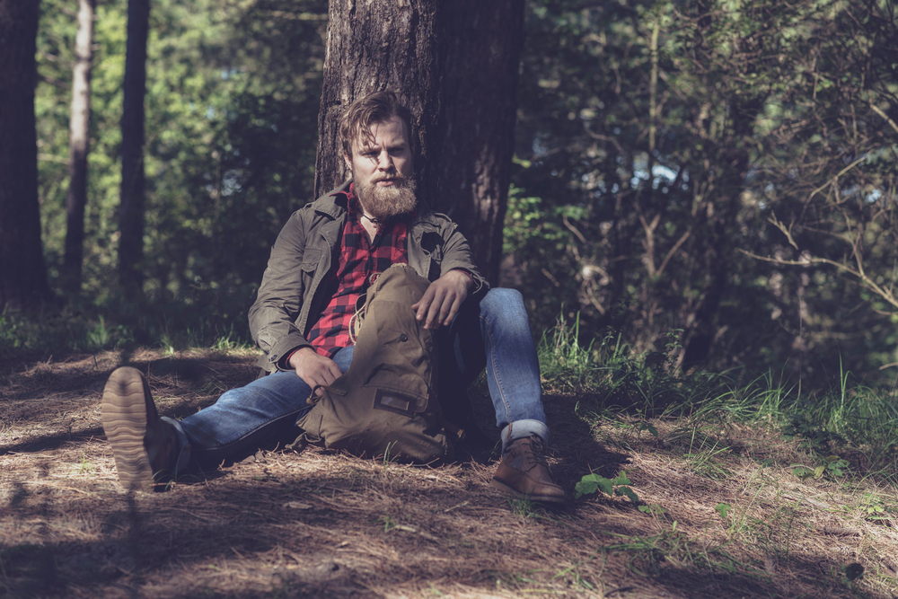 resting hiker in forest sitting against tree.